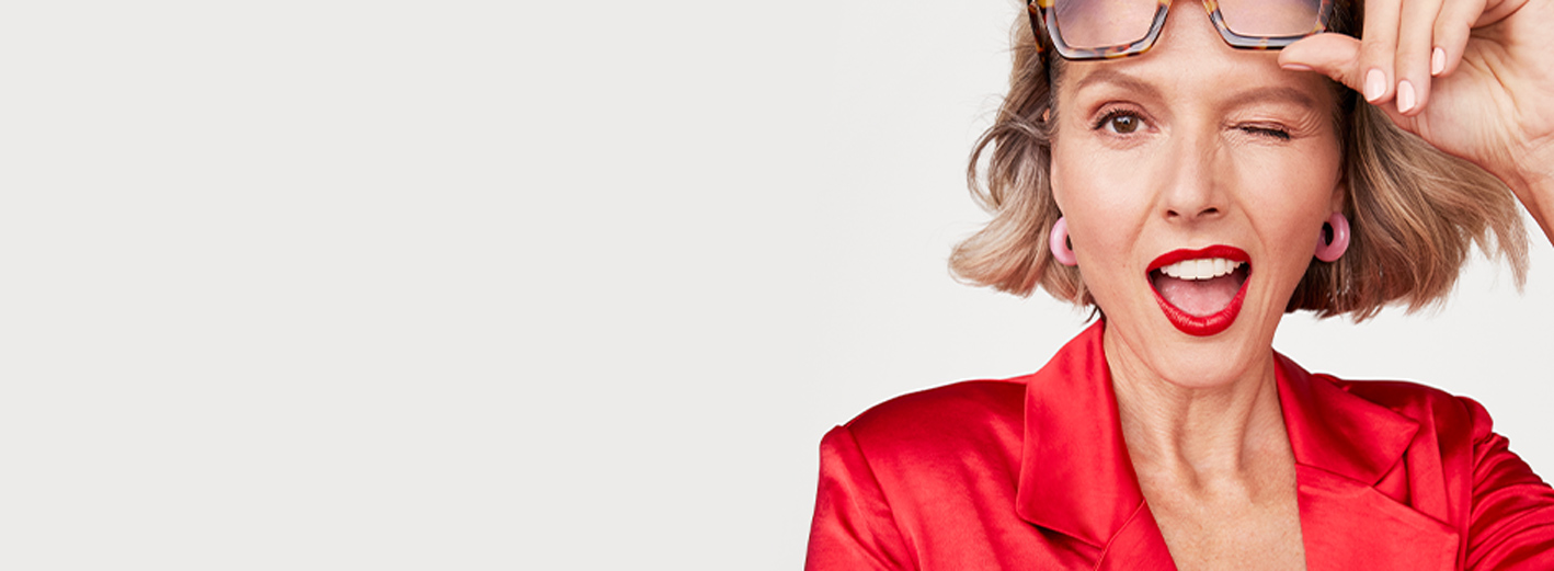 Close up of model playfully lifting her glasses and winking wearing the Classic Confidence makeup artist look