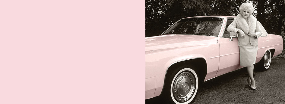Mary Kay Ash leans against a classic pink Cadillac while wearing a pink fur-trimmed dress suit.