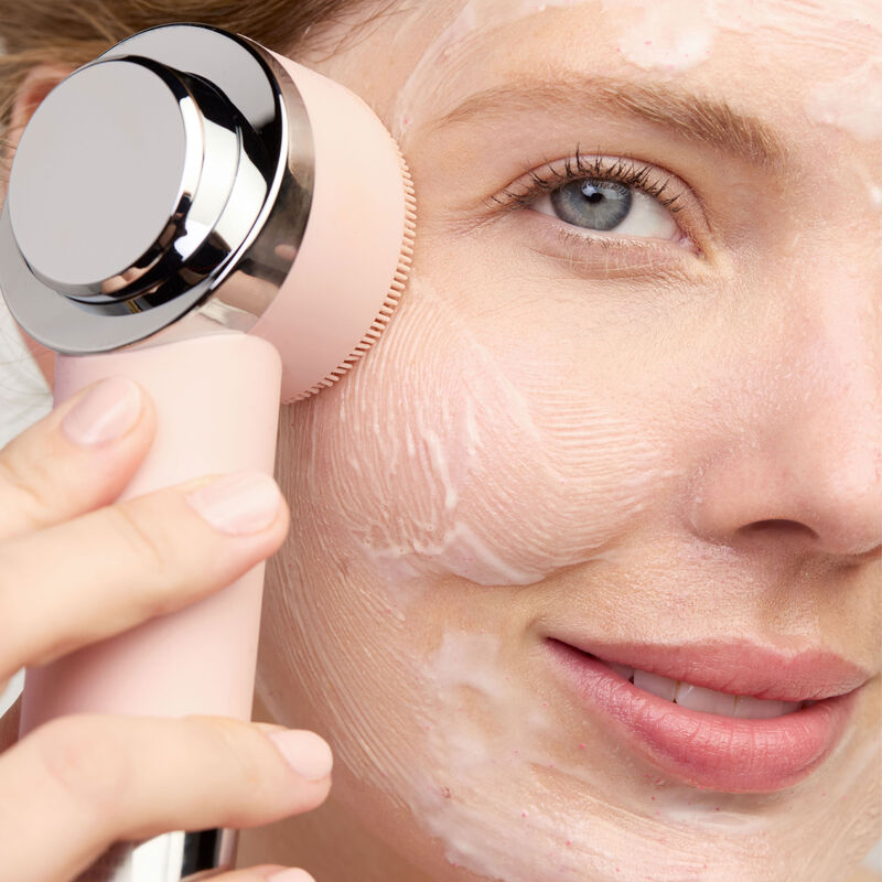 Modelo utilizando la funci&oacute;n limpiadora del Skinvigorate Duo mientras aplica una limpiadora en su rostro