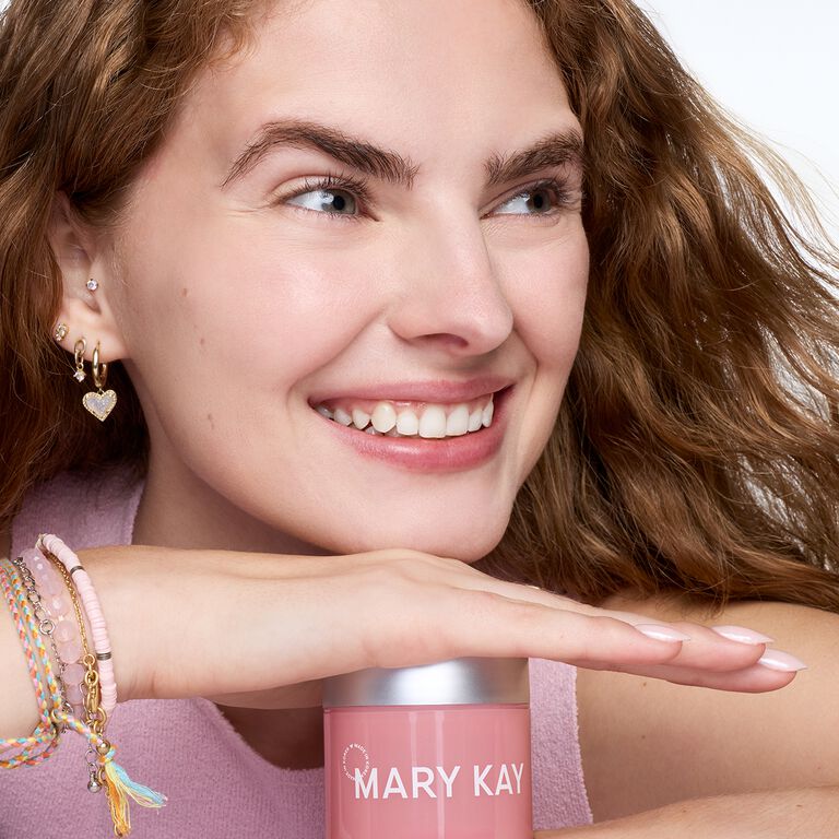 Mujer sonriente apoyando la mano y la cabeza sobre un tarro de gel hidratante con col&aacute;geno de Mary Kay