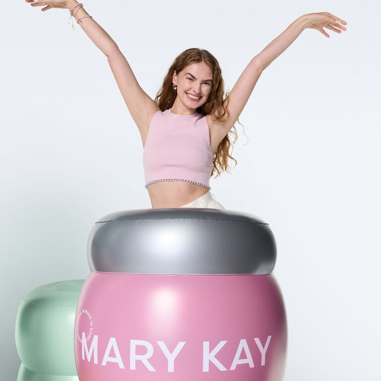 Mujer celebrando detr&aacute;s de un tarro gigante de gel hidratante con col&aacute;geno de Mary Kay