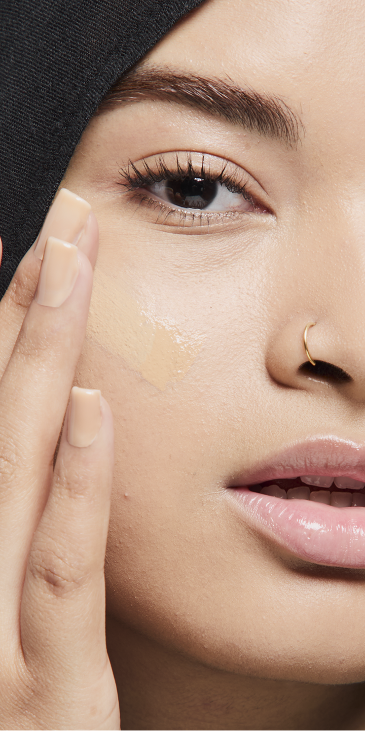 Modelo de tono de piel medio aplic&aacute;ndose base de maquillaje.