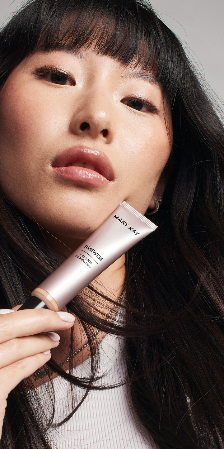 Modelo asi&aacute;tica sosteniendo el producto de base de maquillaje mientras mira a la c&aacute;mara con confianza