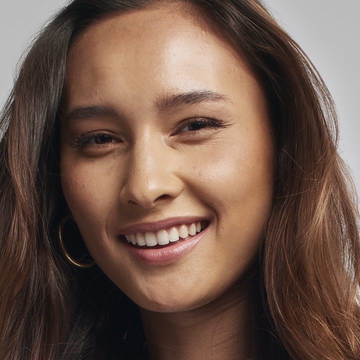 Modelo de cabello casta&ntilde;o sonriendo a la c&aacute;mara mientras lleva puesto su tono de base luminosa