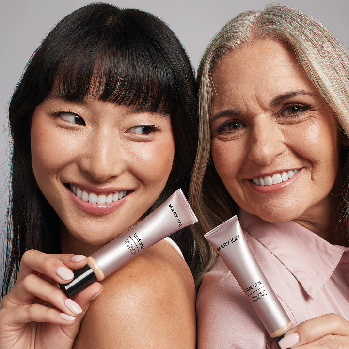Una modelo asi&aacute;tica y una modelo madura sonr&iacute;en mientras se pasan el producto de base de maquillaje